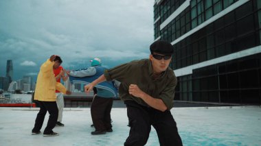 Profesyonel Asyalı dansçı B boy dansı yaparken çok kültürlü arkadaşlar çatıda dans ediyor. Genç modern dans grubu hip hop hareketi yapıyor. Tarz, moda, aksiyon. Açık hava sporu 2024. Hiphop.