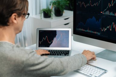 Bilgisayar ve dizüstü bilgisayarı kullanarak, çalışma masasındaki dinamik artırılmış borsa grafiğinin en yüksek kar değerini araştıran bir tüccar, modern ofisteki ekrandaki döviz kuru değerini analiz ediyor. Bireysel.