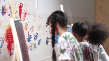 Oyuncu öğrenci resim yapıyor ya da resim dersinde çeşitli arkadaşlarla boyalı duvara resim çiziyor. Dağınık odada çalışan ya da sanat eserleri yaratan mutlu çok kültürlü çocuklar grubu. Yaratıcı aktivite. Etkinlik.