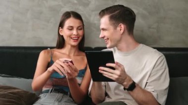 Genç çift, kredi kartıyla ödeme yapabilmek için internet üzerinden ödeme uygulaması ve dijital cüzdan kullanarak yatak odasında oturuyor. Mobil internet üzerinden alışveriş ve modern alımlar. Düzenle