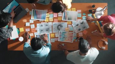 Tasarımcının yukarıdan aşağı görüntüsü renk paletlerini dizüstü bilgisayar ve dizayn ürünleriyle karşılaştırır. Logo grafik tasarımı tartışılırken, pazarlama ekibinin renk seçiminde birlikte çalıştığı hava görüşü. Sempozyum.
