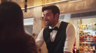 Akıllı barmenin VIP konuğuyla dostça sohbet etmesine odaklanıyorum. Cuma gecesi özel gece partisinde müşterilerin arka tarafındaki lüks tezgahta oturuyorlar. Vinosity.