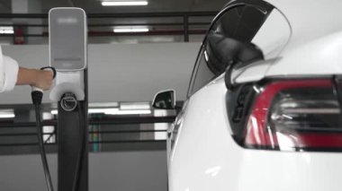Yavaş çekim kadın, EV elektrikli arabasıyla şehir merkezindeki alışveriş merkezinin otoparkına gidiyor. Sürdürülebilirlik yaşam tarzını yeşil, temiz, yeniden şarj edilebilir elektrikli araç iç organlarıyla şarj ediyor.