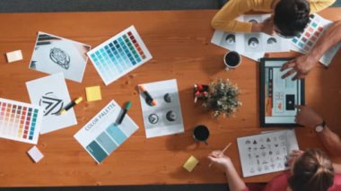 Proje yöneticisi renk paletleri seçerken tasarımcının tablete baktığı yukarıdan aşağıya hava görüntüsü. Profesyonel grafik tasarımının en üst görüntüsü ve logoya bakın. Yetenekli ekip grafikleri seçiyor. Sempozyum.