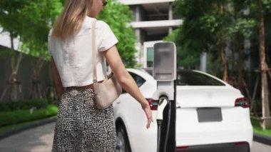 Şehir merkezindeki EV şarj istasyonunda elektrikli araba aküsünü yavaş çekimde şarj eden kadın elektrikli aracın iç organları için sürdürülebilir yeşil ve yenilenebilir temiz enerji yaşam tarzına sahip.