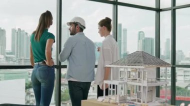 Gökdelene bakıp bir proje planı okurken, günlük kıyafetli akıllı mimar mühendis ekibi konuşuyor. Profesyonel yönetici takımı ev inşaatı hakkında beyin fırtınası yapıyor. Arkadan bak. İzleme