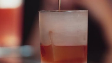 Yakın plan barmen soğuk bardağa karışık viski dolduruyor soğutucu buzlu içecek desenli özel reklam yaratıyor VIP konuk arka planında alkol yenileme gösterisine odaklanıyor. Vinosity.
