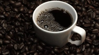 Kahve ya da kahve çekirdekli espresso manzarası. Taze kavrulmuş kahve çekirdeğini yakın çekimde ahşap masanın etrafına bir fincan americano ve aromatik akarsu ve tohum dumanı serpin. Geliştirilebilir.