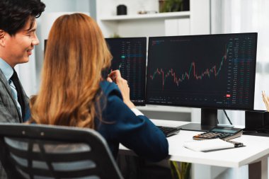 Gülümseyen iş kadını cep telefonunda dinamik borsayı erkek ortağa gösteriyor. Kâr değeri çevrimiçi para birimi çevrimiçi web sitesi programını analiz ediyor. Ofisin arka tarafındaki bilgisayarda karşılaştırıyor. İnfobahn.