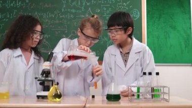 Kafkasyalı öğrenci deney yapıyor ve laboratuvarda yeni yenilikler keşfetmek için bekleyen meraklı çocuklarla çevrili biyokimyasal solüsyon döküyor. Çeşitli mutlu öğrenciler deney yapıyor. Pedagoji.