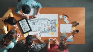 Toplantı odasındaki planlara bakan akıllı mühendisin yukarıdan görünüşü. Yetenekli mimar takımı konuşur ve tartışır. Proje planında planlarla toplantı masasını incelerken. Sempozyum.