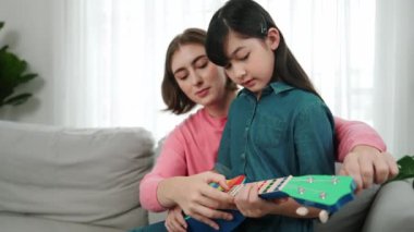 Kafkasyalı bir anne evde akustik müzik öğretirken ukulele çalan mutlu kız. Sevimli çocuk enstrüman öğreniyor. Kafkasyalı mutlu anne ve kız birlikte vakit geçiriyorlar. Pedagoji.