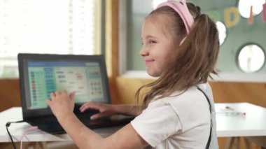 Gülümseyen kız program sistemi ya da STEM teknoloji eğitiminde kodlama programı. Laptop yazma kodunu kullanarak çalışırken kulaklık takan bir çocuk kameraya bakmak için arkasını döner. Etkinlik.