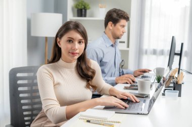 Dizüstü bilgisayarda çalışan gülümseyen güzel bir kadın fotoğraf çekimi için poz verirken modern ofis saatinde akıllı bir iş arkadaşı ile fotoğraf çekimi profili çiziyor. Varsayım.