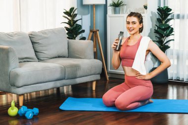 Sportif ve atletik kadınlar spor paspası üzerinde su içiyorlar. Vücut egzersizlerini bitirdikten sonra evde sağlıklı fiziğe ve spor yaşam tarzına uygun bir yaşam sürüyorlar. Gaiety evde egzersiz eğitimi.