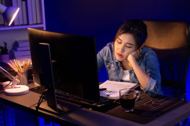Stresli, genç, güzel Asyalı yaratıcı proje yaratıcısı sosyal medyayı araştırmak için bilgisayara bakıyor ve geceleri daha çok neon modern ofisin planlama kanalı stratejisine ulaşılıyor. Taktik.