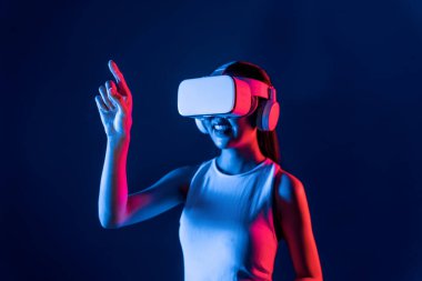Siberpunk neon ışıklı cihazlarla çevrili zeki bir kadın metaevrene bağlı VR kulaklık takıyor, gelecekçi siber uzay teknolojisi. Sanal objeyi işaret eden bir kadın. Halüsinasyon.