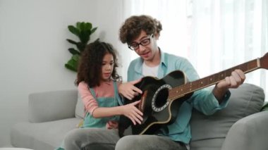 Beyaz bir baba, tatlı kızına koltukta otururken gitar çalmayı öğretiyor. Müzik öğrenirken babasına gitar çalarken bakan tatlı öğrenci kız. Aile eğlence konsepti. Pedagoji.