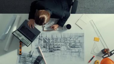 Dizüstü bilgisayar başında çalışırken akıllı mimarın çiziminin zaman aşımı. Kafkasyalı mühendisin bina modelini tasarlayıp, ekipman ve güvenlik kaskıyla birlikte tasarladığına dair tepeden aşağı bir bakış açısı. Hizalama.