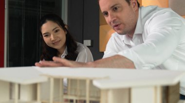 Ev planı çizmek için birlikte çalışan yetenekli mimar mühendisi. Mimar takımı, mimari model, plan ve dizüstü bilgisayarla ofis masasına yerleştirilen ev inşaatı hakkında tartışır. Yönlendirici.