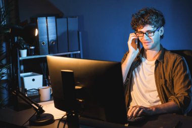 Genç iş adamı akıllı telefondan müşteriyi ya da iş arkadaşını arıyor, neon modern ofisteki yaratıcı sunum surround çalışma masasının bilgisayar ekranına bakıyor. Yeni proje kavramı. Toplayıcı.