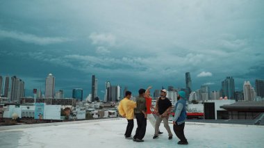 Sokak dansçılarının yakınları dans ederken renkli kıyafetler giyerler. Çekici bir hipster grubu gökdelende ve şehir manzarasında hip-hop müziğine geçecekler. Break dans. Açık hava sporu 2024. Hiphop.