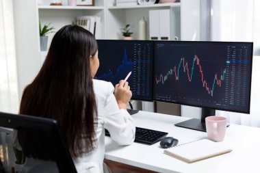 Genç ve güzel Asyalı iş kadını elinde kalemle bilgisayar ekranına bakıyor, modern ofisteki karı analiz ediyor, zenginliğe değer biçilmiş yüksek kârlar yatırıyor. Taktik.