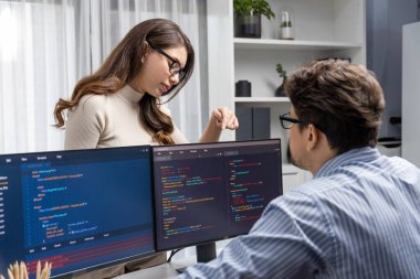 Masada çalışan erkek programcının karşısında duran kadın meslektaşım iki bilgisayar ekranında kodlama web sitesi yazılım sistemi projesini tartışmak için tam yığın veri dizaynı ile karşılaştırıyor. Varsayım.