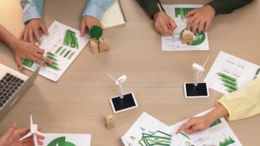 Eko evi projesini yel değirmeni tasarım modeli ve karbon ayak izini azaltmak için yeşil enerji kullanım grafiği ile toplantı masasında tartışan harika bir iş ekibi. Dünyayı kurtarın. Eline odaklan. Tanımlama.