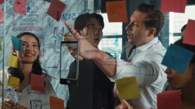 Cam duvarda yaratıcı fikirleri paylaşmak için renkli yapışkan notlar kullanarak pazarlama fikrini değerlendiren mutlu profesyonel iş adamları. Bir grup farklı iş adamları strateji hakkında tartışıyorlar. Yönlendirici.