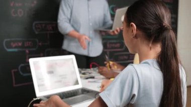 Afrikalı erkek manken tamir ederken beyaz kız programlama ya da kodlama sistemi. Öğretmen elinde dizüstü bilgisayar tutarken çeşitli çocukların web geliştirme programı yazmalarına bakıyor. Yenilik eğitimi. Öğretim