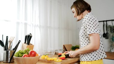 Enerjik anne, mutfak malzemeleri ile çevrili sebzeleri doğrarken modern mutfakta kahvaltı için salata yapıyor. Akıllı kadın temizlikçi yemek pişirir ve yemek hazırlar. Sağlıklı bir yaşam tarzı. Pedagoji.