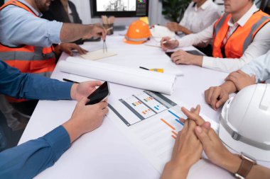 Mimari proje üzerinde birlikte çalışan çeşitli inşaat mühendisi ve müvekkil grupları, inşaat planını gözden geçirip toplantı masasında plan oluşturuyorlar. Tedbirli