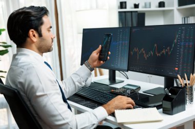 Akıllı telefondan akıllı telefon arayan tüccar işadamı, bilgisayardaki dinamik borsa yatırım ekranını analiz ediyor ve modern merkez ofisteki en kârlı finansal teknoloji pazarına yatırım yapıyor. Tahmin et..