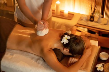 Sıcak bitkisel top spa masaj vücut tedavisi, masör kadın vücuduna nazikçe şifalı bitki torbası bastırıyor. Aromaterapi tesisinin sakinliği ve dinginliği kaplıca salonundaki mumların sıcacık ışığında. Sessiz.