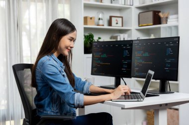 IT geliştiricisinde gülümseyen genç Asyalı dizüstü bilgisayarında kodlama programı verileriyle kotlu tişört giyerek çevrimiçi bilgi yazıyor. Güvenlik analizi iki ekran ile çevrili. Taktik.