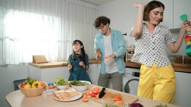 Kafkasyalı anne ukulele çalarken ve mutfakta müzik dinlerken mutlu aile dansları. Asyalı kız mutfakta şarkı söyleyip dans ederken akıllı ebeveynlerle yemek pişirmeye hazırlanıyor. Pedagoji.