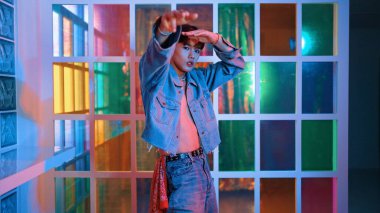 Gece kulübünde kameraya bakarken güneş gözlüklü Asyalı sanatçının serbest dans edişini yakından çek. Mutlu sokak dansçısı dans ediyor ve renkli parlak neon ışıklı ayak izlerini gösteriyor. Mutluluk.