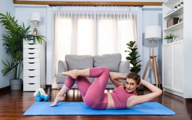 Flexible and dexterity woman in sportswear doing yoga position in meditation posture on exercising mat at home. Healthy gaiety home yoga lifestyle with peaceful mind and serenity. clipart