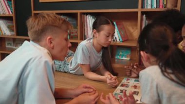 Akıllı kız, çocuk kütüphanede çeşitli arkadaşlarıyla konuşurken resimli kitaba bakıyor. Bir grup çocuk kitabı paylaşırken sevimli bir lise öğrencisi kitaplığın yanında daireler çizerek yatıyor. Öğretim