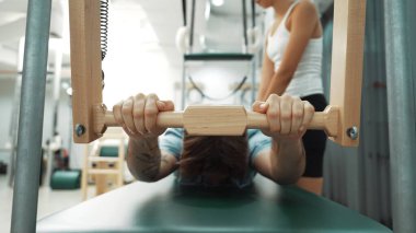 Eğitmen rehberliğinde Pilates Cadillac üzerine bar tabanlı alıştırma yapan bir müşteri. Erkek öğrenci, üst vücut gücünü arttırmak için Cadillac 'ın üzerinde kuğu esnetiyor. Alışkanlık.