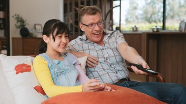 Grandfather and granddaughter together watch interesting entertainment media on TV. Old senior use technology communicate with young generation cross generation gap strengthen family bond. Divergence. clipart