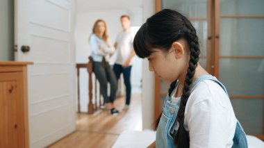 Stresli ve mutsuz genç kız köşeye kıvrılıp kulaklarını kapatarak arka planda ebeveyninin tartışmasını engelliyor. Evde aile içi şiddet ve travmatik çocukluk depresyona dönüşür. Eşzamanlama