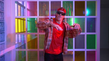 Komik break dansçı kameraya bakarken hiphop 'a doğru serbest adım atıyor. Çılgın mutlu hipster dans edip sokak dansı yaparken Led ışığında günlük kıyafet ve güneş gözlüğü takıyor. Mutluluk.