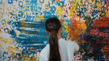 Genç mutlu kız renk tepsisini tutuyor ve fikri ifade etmek ve el iziyle hayal gücünü geliştirmek için renkli duvarları boyuyor. Resim dersinde odayı dekore etmek için beyaz kız pulu. Öğretim.