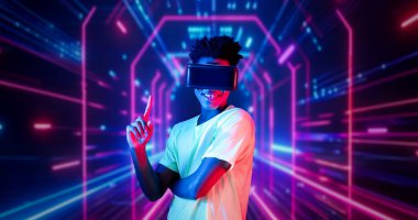 VR gözlüklü profesyonel erkek oyuncu parlayan neon ışıkla oyun oynuyor. Heyecanlı oyuncu artırılmış gerçeklik teknolojisi yeniliklerini kullanarak metaevrene bağlanmayı seviyor. Yaratıcılık.
