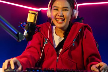 İnternet üzerinden kulaklık takıp gülümseyen Asyalı güzel kız flamasının sunucu kanalı izleyicilerle internet üzerinden konuşma yapıyor. Esport yetenekli takım oyuncuları neon mavi odada. Taktik.