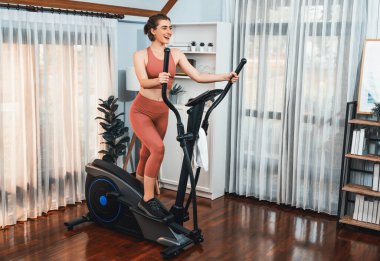 Spor ve atletik bir kadın, evdeki fiziğe ve sağlıklı spor yaşam tarzına uygun vücut egzersizi sırasında eliptik koşu makinesiyle koşuyor. Gaiety evde egzersiz eğitimi.