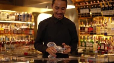İyi görünümlü, gülümseyen Asyalı, zeki barmen, lüks içki tezgahı sahnesinde bardakları siliyor. Profesyonel barmen kostümü içinde, gece kulübü konforuna sıcak bakıyor. Vinosity.