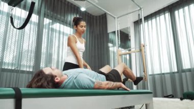 Cadillac ekipmanları üzerinde bacak kaldırma egzersizinde müşteriye yardımcı olan yetenekli pilates eğitmeni. Kadın antrenör, Cadillac 'ın bacak gerdirme hareketine yardım ediyor. Temel bağlantıyı geliştirmek için, bacak esnekliği için. Alışkanlık.